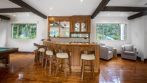 Une pièce spacieuse avec un bar en bois, des tabourets de bar, une table de billard et un coin salon comprenant un canapé et des fauteuils.