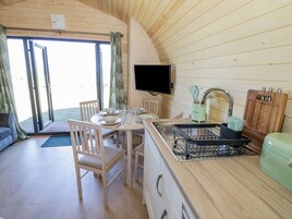 Una cocina compacta con armarios de madera, una mesa de comedor con sillas, un lavabo con escurreplatos y un televisor montado en la pared.