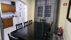 A dining area with a black table and wooden chairs, a kitchen with wooden cabinets and a white dishwasher, and a fire extinguisher on the floor.
