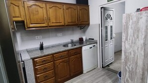 A kitchen with wooden cabinets, a granite countertop, a white dishwasher, and a door with a frosted glass panel.