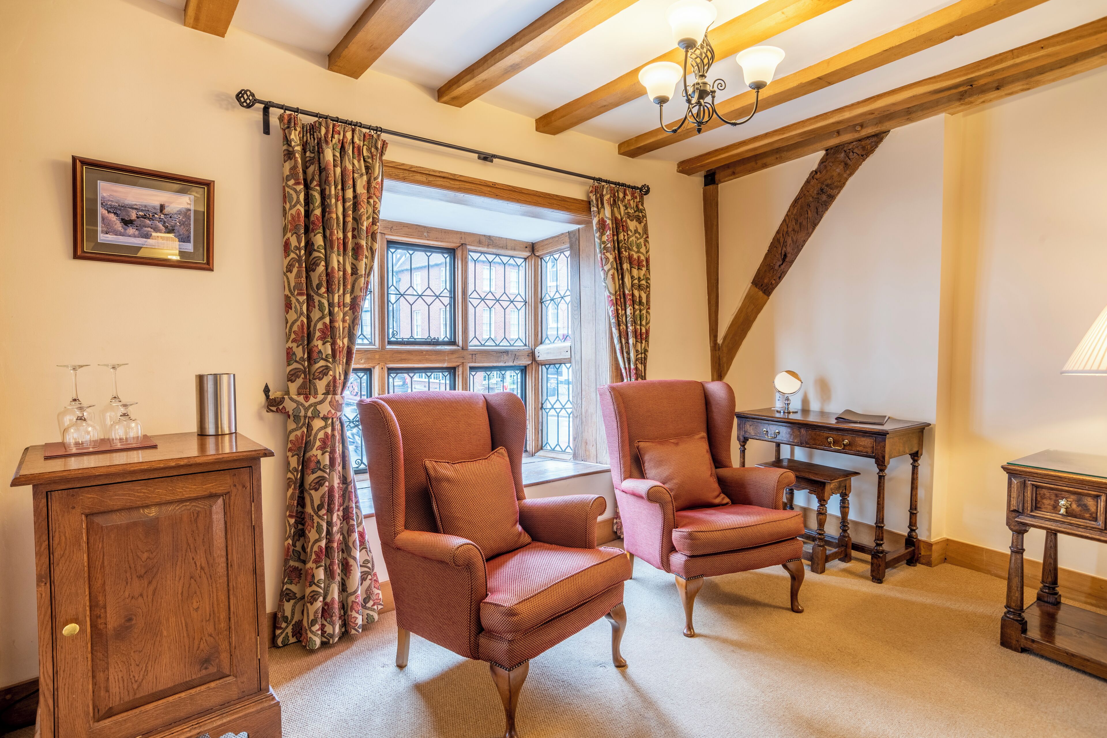 A cozy room with two armchairs, a wooden cabinet, and a desk with a lamp.
