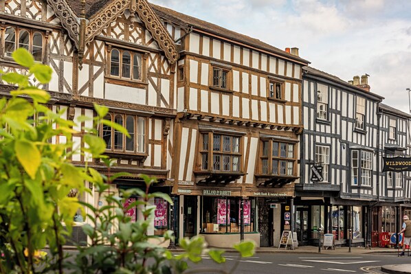 A traditional half-timbered building with multiple shops on the ground floor, including a butcher and a health food store. - Townhouse Ludlow (Ludlow)