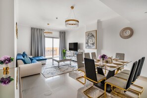Relax in this stylish living area with a comfortable sofa, flat-screen TV, and dining space featuring a glass-top table and elegant chairs.