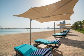 Relax in comfort with lounge chairs and sunbeds shaded by large umbrellas, overlooking the beach.