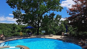 A swimming pool with a hot tub, surrounded by lounge chairs and umbrellas, with trees in the background. - Modern Vibe, 5 Beds, 6 pools, Great Location (Lake Ozark)