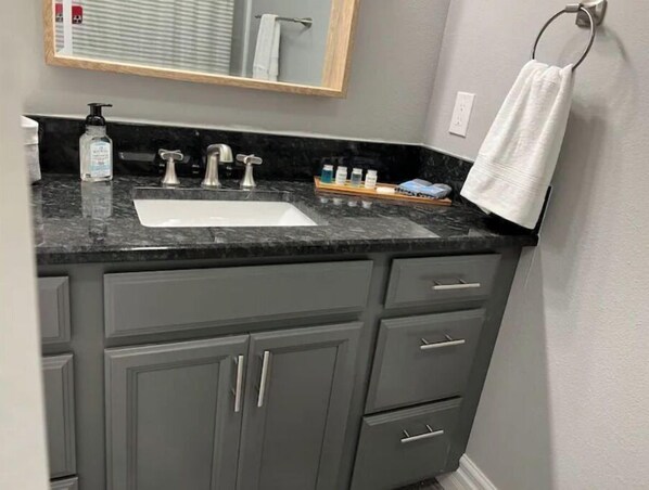 Une salle de bain avec un comptoir en marbre, un lavabo et un miroir au-dessus.