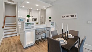 Une cuisine moderne avec des meubles blancs, un coin repas doté d’une table en bois foncé et un escalier menant à un autre niveau.