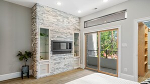 Une chambre avec un mur d’accent en pierre, un téléviseur fixé sur ce mur, une porte-fenêtre coulissante donnant sur un balcon et un lit recouvert d’une couverture à rayures.