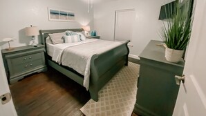A bedroom with a bed, bedside tables, a nightstand, a ceiling fan, a window with blinds, a wall-mounted TV, and a potted plant. - Cozy Bungalow, close to the lake.  (Graford)