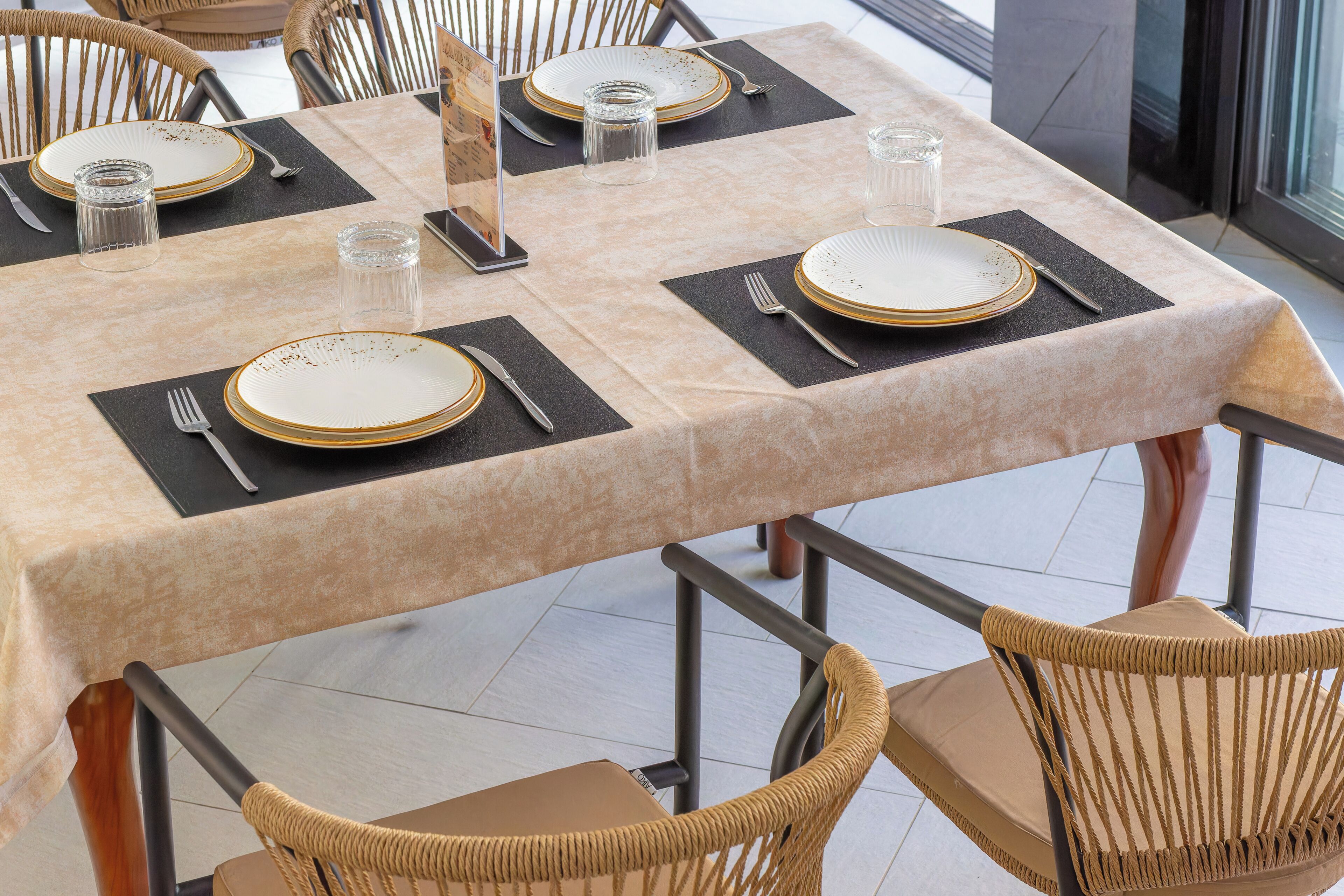 A dining table set with plates, cutlery, and glasses, surrounded by wicker chairs.