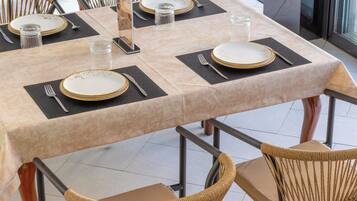 A dining table set with plates, cutlery, and glasses, surrounded by wicker chairs.