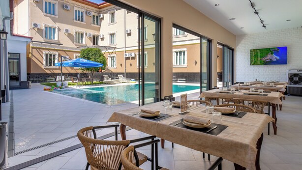 A restaurant with outdoor seating overlooking a swimming pool, large windows, and a flat-screen TV on the wall. - Grand Nur (Tashkent)