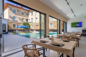 A restaurant with outdoor seating overlooking a swimming pool, large windows, and a flat-screen TV on the wall. - Grand Nur (Tashkent)