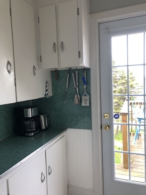 Una cocina con armarios blancos, una cafetera y una puerta con ventana que da a una terraza.