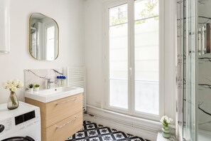 Ein modernes Badezimmer mit einem weißen Waschtisch, einem Spiegel, einem Heizkörper und einem großen Fenster.