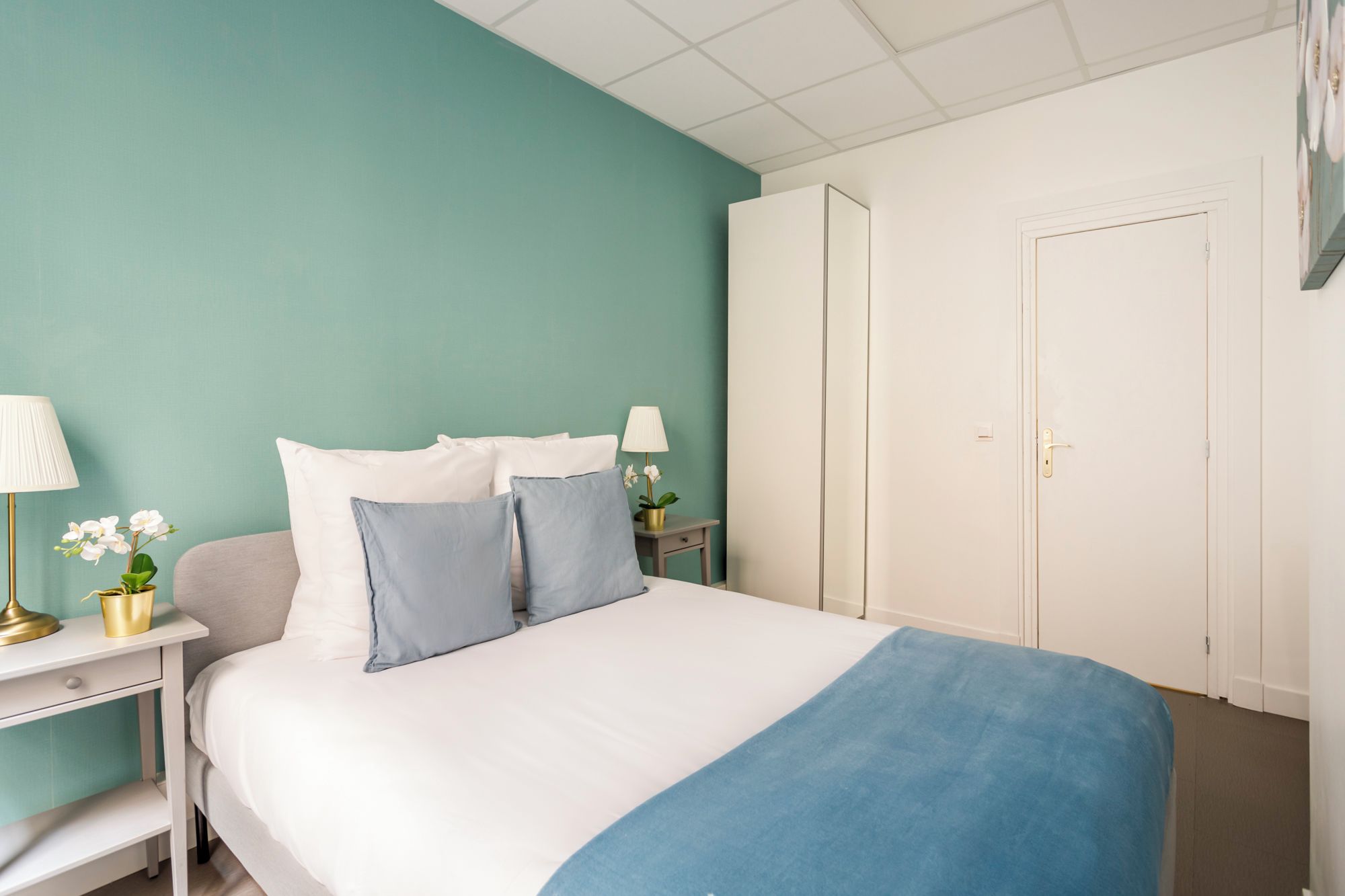 A neatly arranged bedroom with a bed, bedside tables, lamps, and a wardrobe.