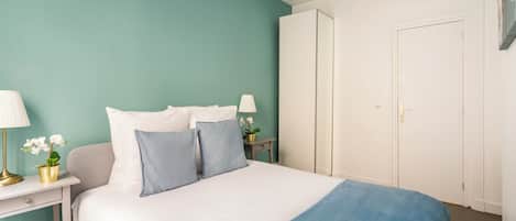 A neatly arranged bedroom with a bed, bedside tables, lamps, and a wardrobe.