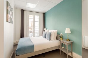 A neatly arranged bedroom with a bed, bedside table, and a window with curtains.