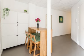 A modern, minimalist room with a wooden dining table and chairs, a vase with pink flowers, and a green plant on a white cabinet. - Family Suite - Marais - Turbigo I (Paris)