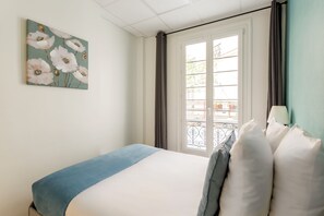 A bedroom with a bed, a window with curtains, and a painting on the wall. - Family Suite - Marais - Turbigo I (Paris)
