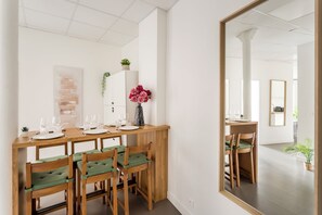A dining area with a wooden table set for six, six chairs with green cushions, a vase with pink flowers, and a white cabinet with a plant. - Family Suite - Marais - Turbigo I (Paris)