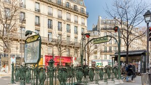 Une scène de rue avec des grilles en métal décoratives, un panneau d’arrêt de tramway et un autobus rouge en arrière-plan.