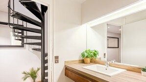 Une salle de bain moderne avec un meuble-lavabo en bois, un lavabo blanc, un grand miroir et un escalier en colimaçon noir.