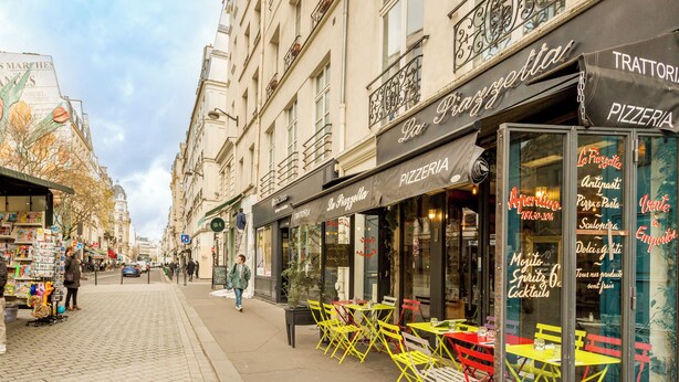 Une rue avec des terrasses et une pizzeria.