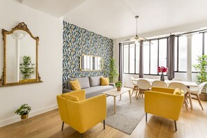 Un salon moderne avec un canapé, des fauteuils jaunes, une table à manger et une grande fenêtre avec des rideaux.