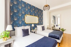 A hotel room with two beds, a large mirror, a potted plant, and a nightstand with a lamp. - Merveil - Family Suite - Louvre - Sentier I (Paris)