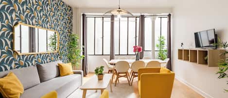 A modern living room with a sofa, yellow armchairs, a dining table, and a TV.