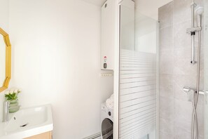 Une salle de bain moderne avec un lavabo blanc, un miroir, une douche avec une porte en verre et un lave-linge.