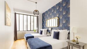 Een hotelkamer met twee bedden, een groot raam met gordijnen, een radiator, een nachtkastje met een lamp en een spiegel aan de muur.