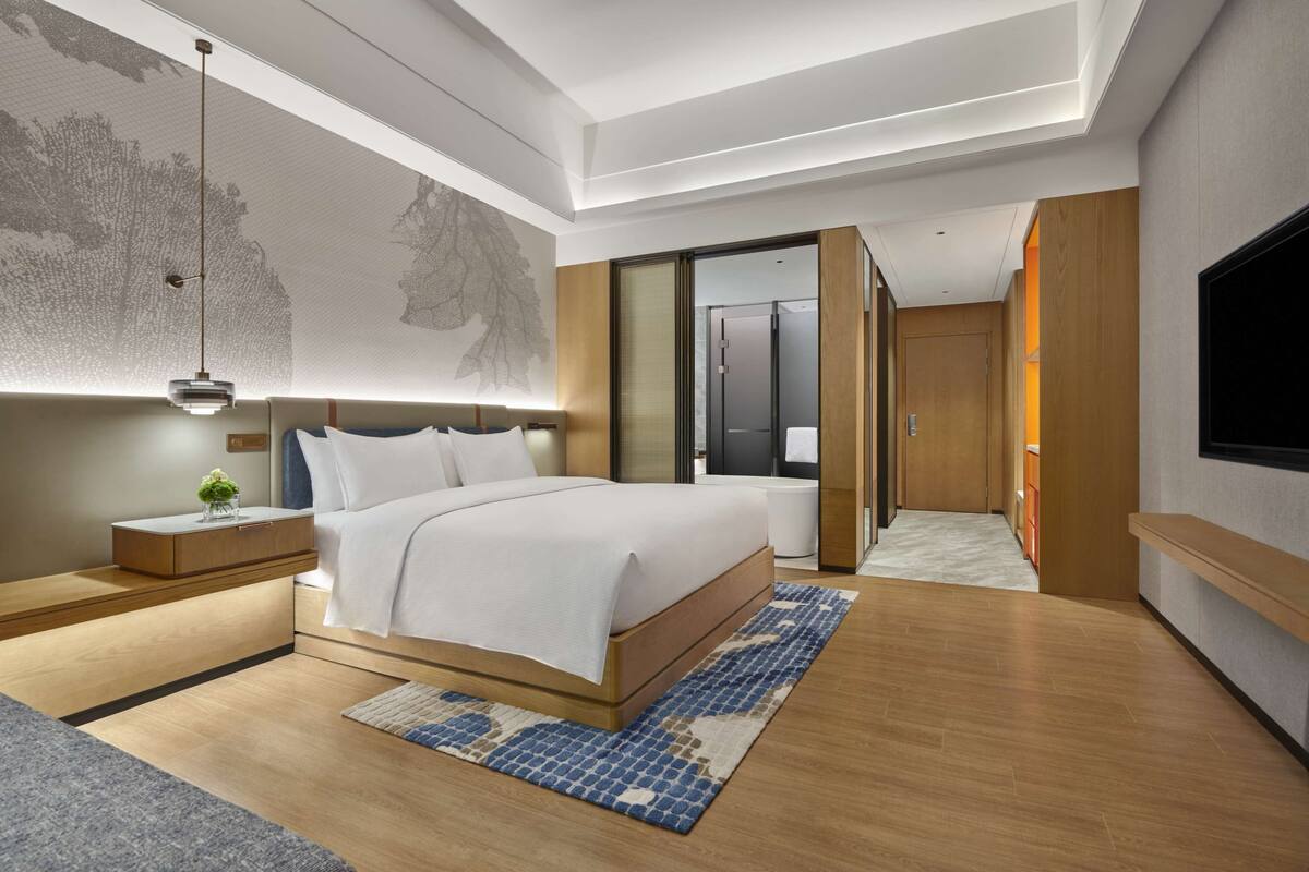 A modern hotel room with a large bed, bedside tables, a TV, and a walk-in closet.