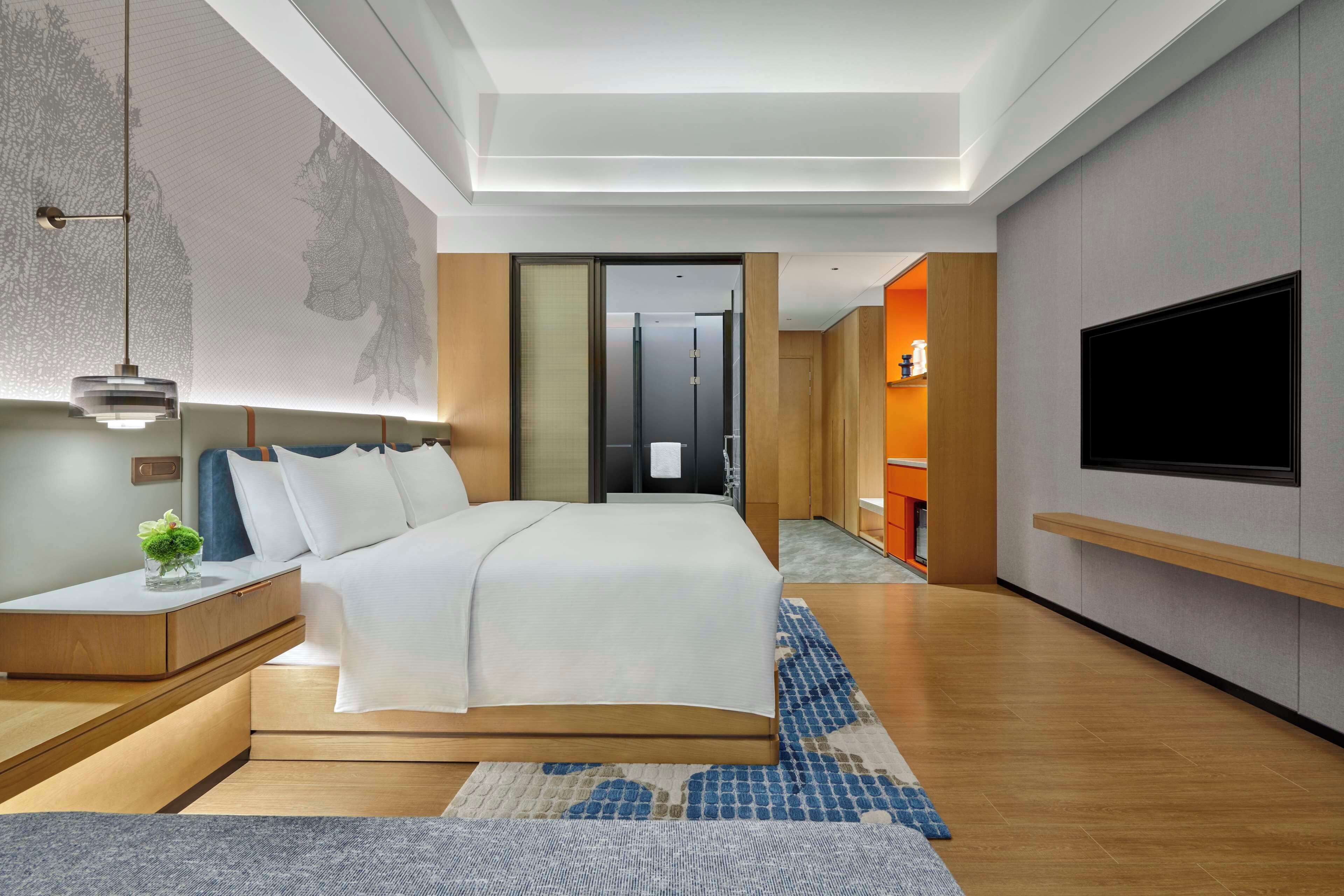 Une chambre d’hôtel moderne avec un grand lit, une table de chevet et un téléviseur fixé au mur.
