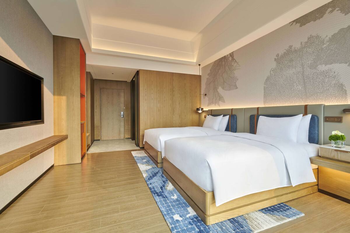 A modern hotel room with a large bed, a flat-screen TV, a wooden accent wall, and a decorative wall mural.