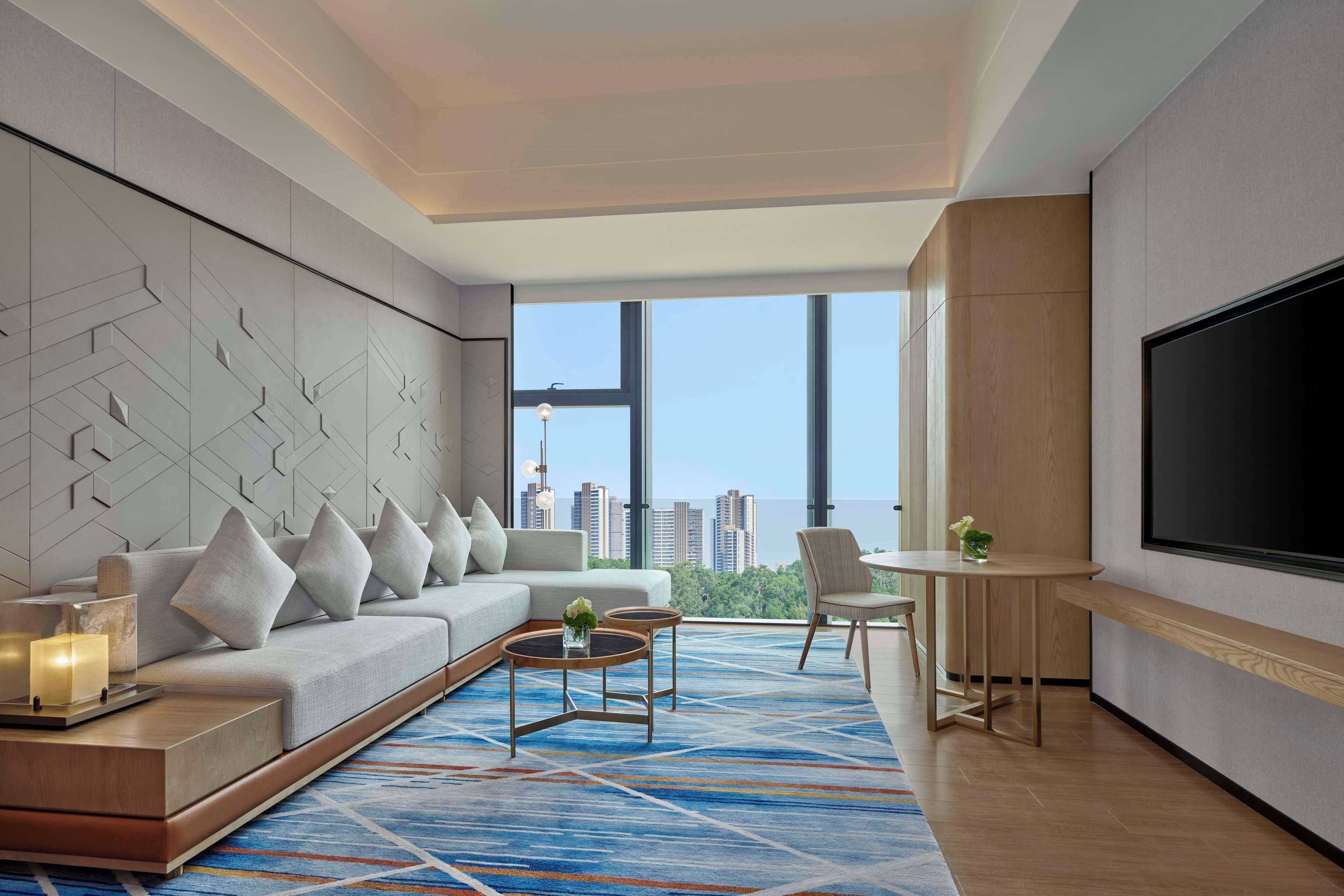 Une chambre d’hôtel moderne dotée d’une grande fenêtre, d’un canapé, d’une table basse, d’un téléviseur et d’un coin repas.