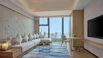 Une chambre d’hôtel moderne dotée d’une grande fenêtre, d’un canapé, d’une table basse, d’un téléviseur et d’un coin repas.