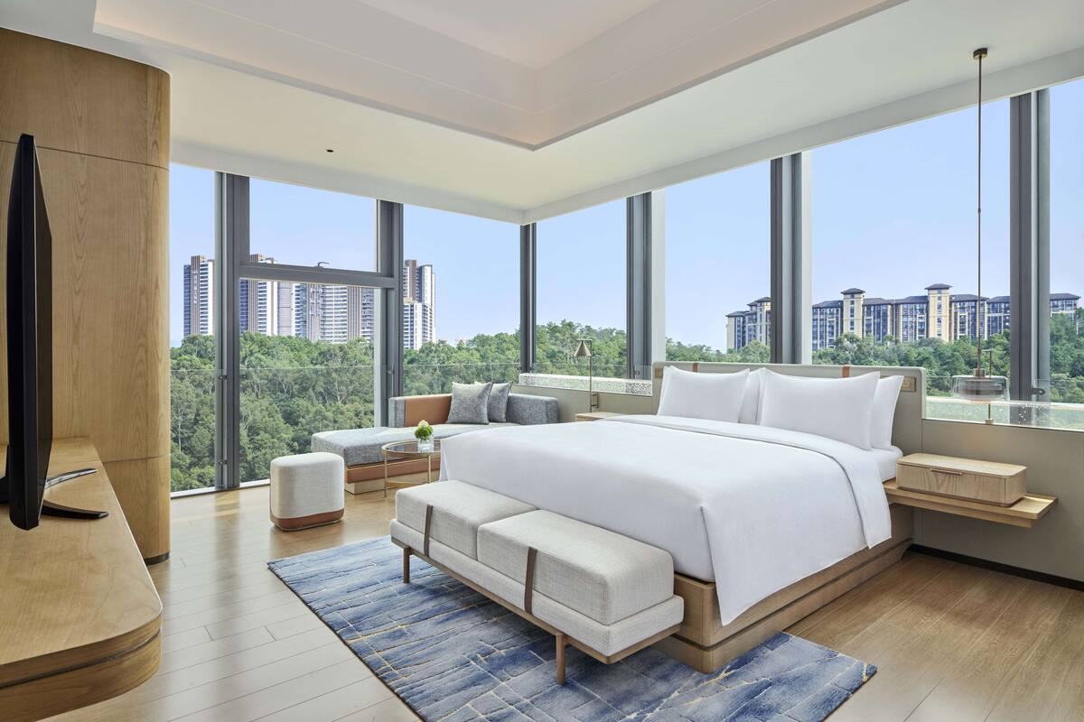 A modern bedroom with a large bed, a wooden desk, and a view of the city.