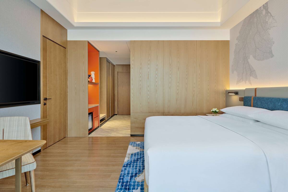 A modern hotel room with a large bed, wooden flooring, a flat-screen TV, and a small table with a chair.