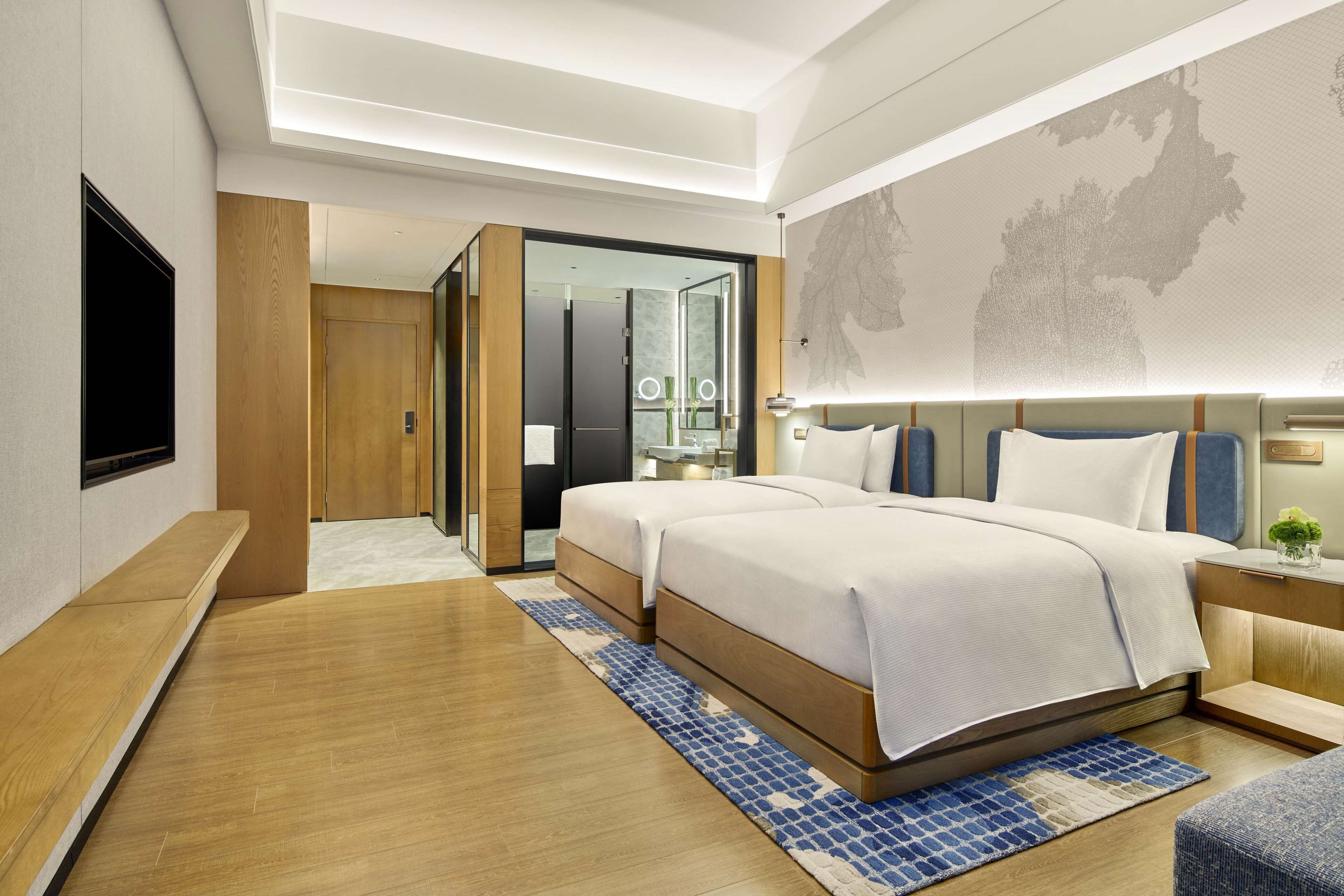 A modern hotel room with a large bed, a flat-screen TV, wooden flooring, and a map on the wall.