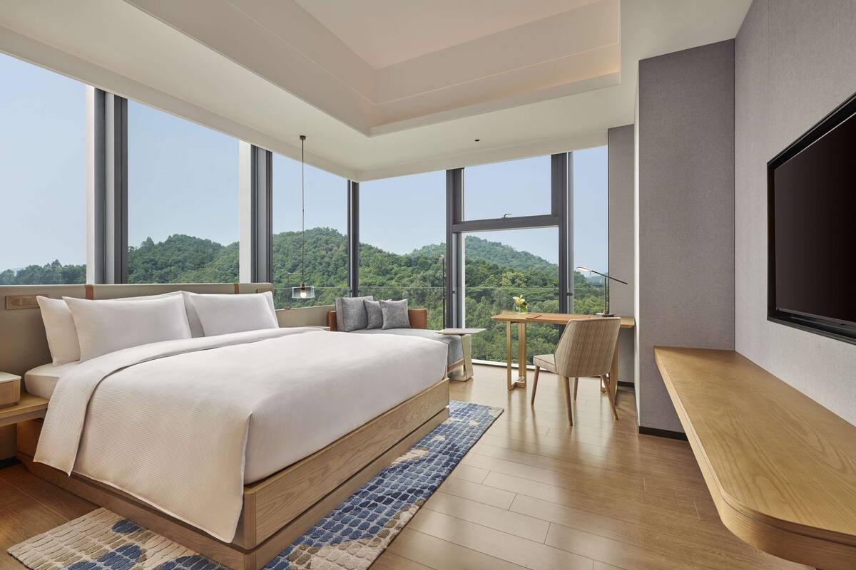 A modern bedroom with a large bed, a desk, and a TV.