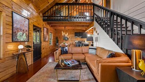 A spacious living room with a large sofa, a coffee table, and a staircase leading to an upper level. - Ridgetop VIEWS! Arcade+Hot Tub+Fire Pit+Privacy (Sevierville)