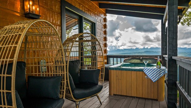 A wooden deck with a hot tub, wicker chairs, and a view of the mountains. - Ridgetop VIEWS! Arcade+Hot Tub+Fire Pit+Privacy (Sevierville)
