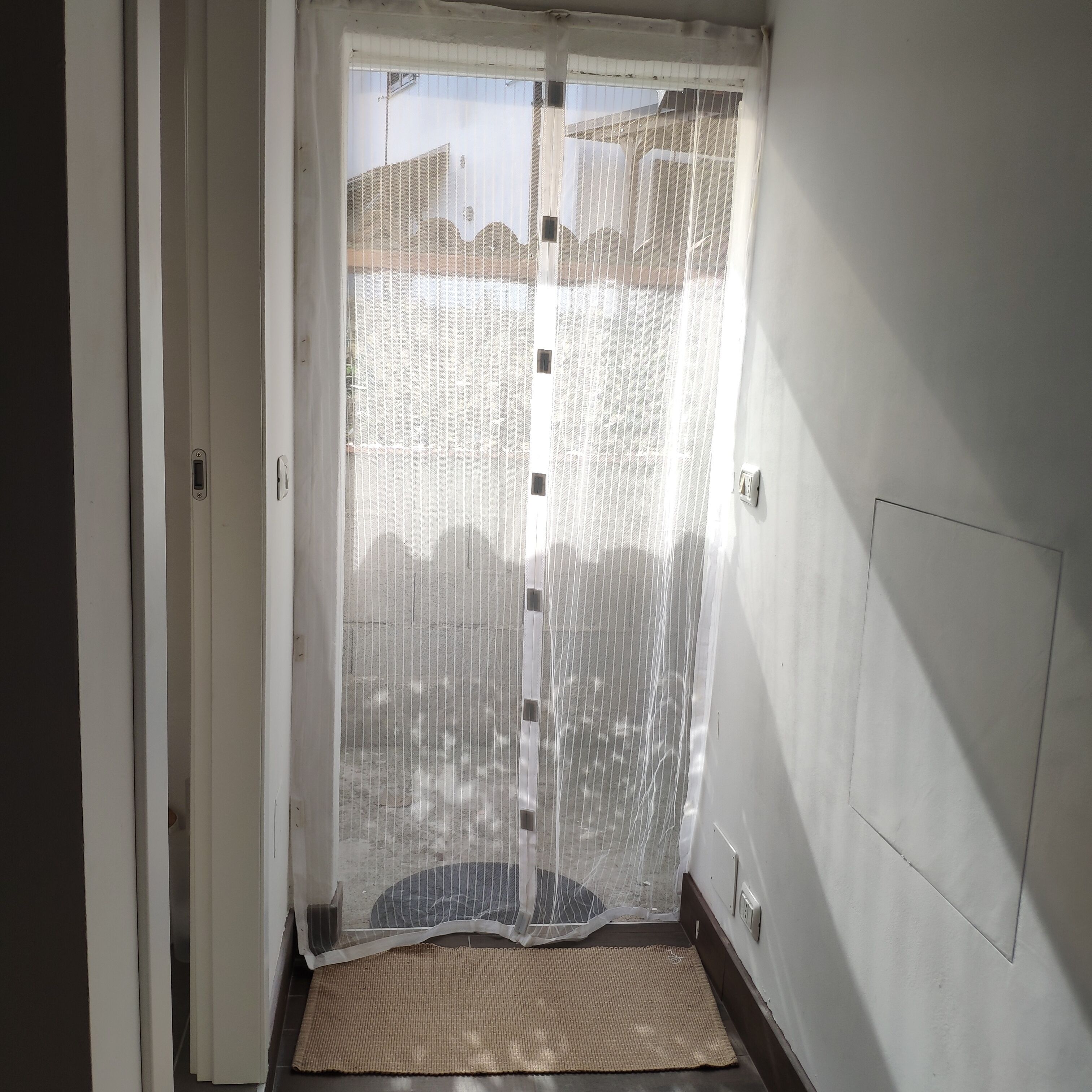 Ein Zimmer mit einer Schiebeglastür, einem kleinen Teppich auf dem Boden und einem an der Wand montierten Lichtschalter.