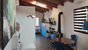 Une pièce avec un plafond en bois, une table à manger avec des chaises, un buffet bleu et un tuyau noir.