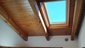 Une chambre avec un lit superposé, une lucarne, des poutres en bois et un panier en osier.