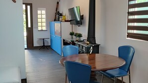 Un coin repas avec une table en bois et des chaises bleues, une cuisine avec un poêle noir et un téléviseur fixé au mur.