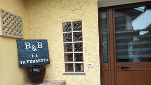 L’entrée d’un immeuble, avec une enseigne indiquant « B&B TAVERNETTA » et une grande plante en pot.