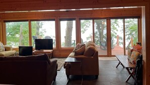 Un interior de cabaña acogedor con un ventanal grande, un sofá, un televisor y una mesa de comedor.
